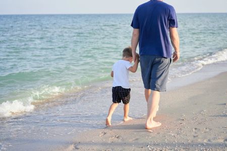 Eine Vater mit seinem Sohn spazieren barfuß am Strand